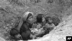 A Cambodian woman with five children apprehensively looks upwards from the shallow bunker as shells from the insurgent forces start falling in the area in the encircled capital of Phnom Penh, in March 1975.