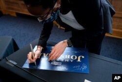 FILE - Kim Lewis, an associate dean at Howard University in Washington, autographs an American Jobs Plan sign after participating with Energy Secretary Jennifer Granholm in a discussion at the university, May 3, 2021.