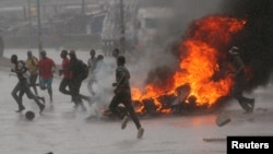 People run at a protest as barricades burn during rainfall in Harare