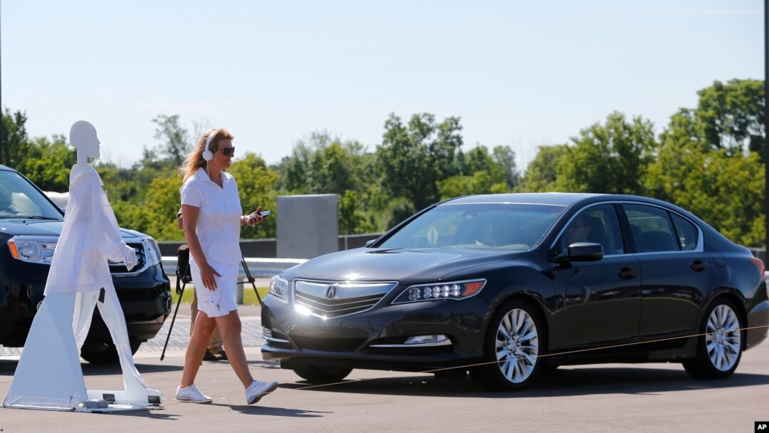 FILE - A pedestrian crosses in front of a vehicle as part of a demonstration at the Mcity test facility at the University of Michigan in Ann Arbor, July 20, 2016. Automakers say cars that wirelessly talk to each other hold the potential to dramatically reduce traffic deaths.