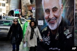 FILE - Women walk past a banner of Iranian military commaner Qassem Soleimani, who was killed in Iraq in a U.S. drone attack, in Tajrish square in northern Tehran, Iran, Jan. 9, 2020.