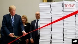 President Donald Trump cuts a ceremonial red tape during an event on federal regulations at the White House, Dec. 14, 2017, in Washington. "Let's cut the red tape, let's set free our dreams," Trump said, next to stacks of paper that he said represented the size of the federal regulatory code.