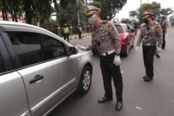 Police officers check the number of people seated inside a car during the imposition of large-scale social restriction, at a checkpoint in Jakarta, Indonesia, April 10, 2020.