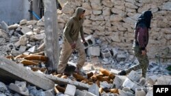 Fighters of the US-backed Kurdish-led Syrian Democratic Forces walk through debris and mortar shells in the village of Baghuz in the eastern Syrian province of Deir Ezzor on March 21, 2019.