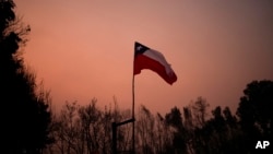 Una bandera chilena colocada en medio de árboles carbonizados bajo un cielo rojo causado por incendios forestales en Santa Juana, Chile, el 5 de febrero de 2023. 