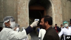 An Afghan health worker, left, takes the temperature of a guest to check for coronavirus at the entry gate of presidential palace during in an inauguration ceremony for President Ashraf Ghani in Kabul, Afghanistan, March 9, 2020. 