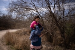 María, una niña salvadoreña de 4 años, es llevado en los hombres de su mamá Loudi, mientras avanza a pie por un camino de tierra después de cruzar el río Grande hacia Estados Unidos desde México en Penitas, Texas, EE. UU., 5 de marzo de 2021.