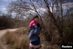 María, una niña salvadoreña de 4 años, es llevado en los hombres de su mamá Loudi, mientras avanza a pie por un camino de tierra después de cruzar el río Grande hacia Estados Unidos desde México en Penitas, Texas, EE. UU., 5 de marzo de 2021.