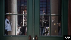 FILE - Law enforcement officers look on through Ohio Statehouse doors as people rally outside to protest the stay-at-home order in Columbus, Ohio, April 20, 2020.