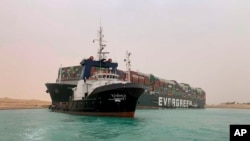 In this photo released by the Suez Canal Authority, a boat navigates in front of a massive cargo ship, named the Ever Green, rear, grounded, March 24, 2021, after it turned sideways in Egypt’s Suez Canal.