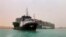 In this photo released by the Suez Canal Authority, a boat navigates in front of a massive cargo ship, named the Ever Green, rear, grounded, March 24, 2021, after it turned sideways in Egypt’s Suez Canal.