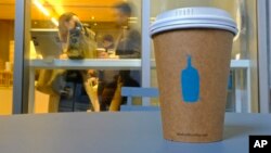 In this Thursday, Dec. 12, 2019 photo, a Blue Bottle Coffee paper to-go cup rests on a table outside one of their cafes in San Francisco. The Oakland-based chain says it's getting rid of disposable cups at two locations next year, as part of a pledge to g