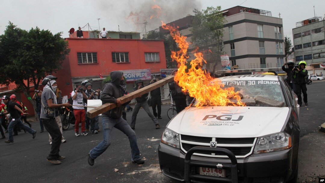 Para pemrotes membakar mobil polisi saat berunjuk rasa di Mexico City, Kamis (20/11).