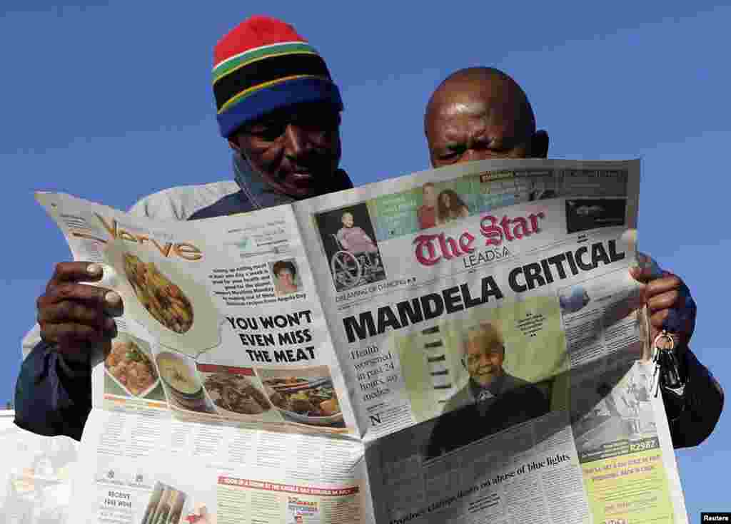 Men read a newspaper next to a stall in Soweto June 24, 2013. South Africans appeared resigned on Monday to the inevitability of one day saying goodbye to former president Nelson Mandela after the 94-year-old anti-apartheid leader's condition in hospital 