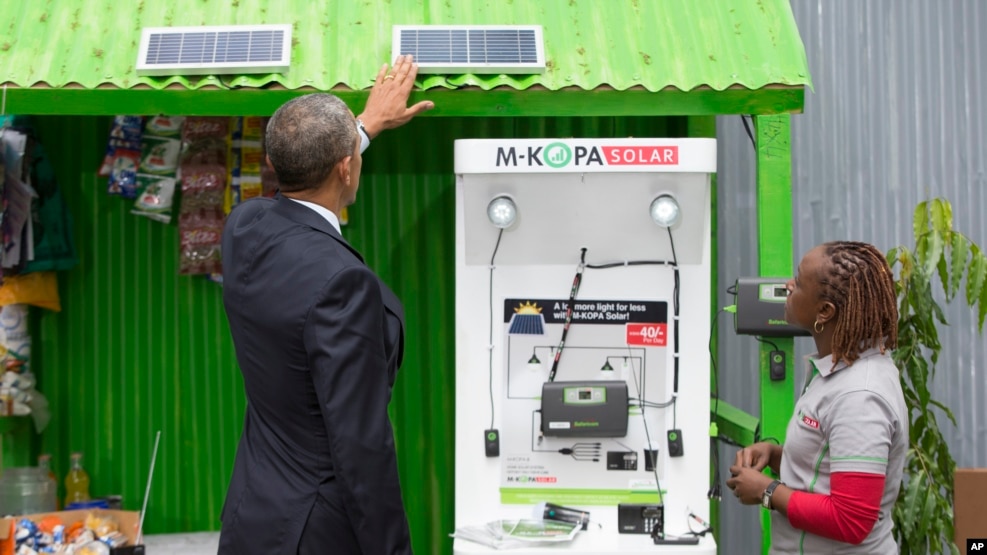 FILE - Then-President Barack Obama looks at a solar power exhibit during a tour of the Power Africa Innovation Fair, July 25, 2015, in Nairobi, Kenya. With technical help from the U.N. Industrial Development Organization, a cooperative in Olosho-Oibor installed solar panels on poles around the community and on rooftops. It has installed two small wind turbines as well.