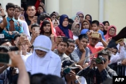 Onlookers watch as a member of Indonesia's Sharia police, at right outside the frame, whips a non-Muslim woman, bottom left, for trading alcohol during a public caning ceremony outside a mosque in Banda Aceh, the capital of Aceh province, July 13, 2018.