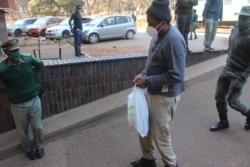 In handcuffs and leg irons, journalist Hopewell Chin’ono arriving at the Harare Magistrates Court, Aug. 19, 2020, for his third bail attempt with another official from Zimbabwe Lawyers for Human Rights. (Columbus Mavhunga/VOA)