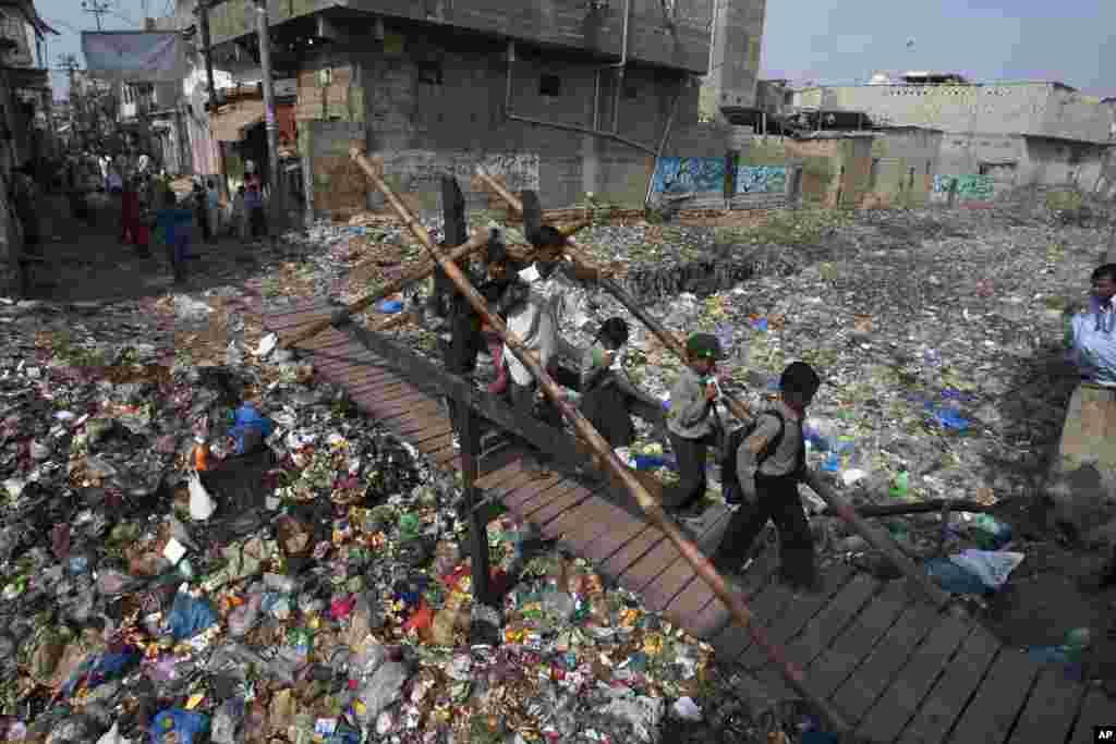 School children cross a makeshift pedestrian bridge over a drain covered with garbage at a slum in Karachi, Pakistan.