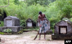 FILE - A worker cleans the ground near the graves at a Jewish cemetery located on the edge of Rangoon, Oct. 2006.