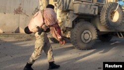 FILE - An Afghan security personnel carries a wounded man after a suicide car bomb blast attacked a military convoy in Lashkar Gah, Helmand province, Afghanistan, Nov. 15, 2015.