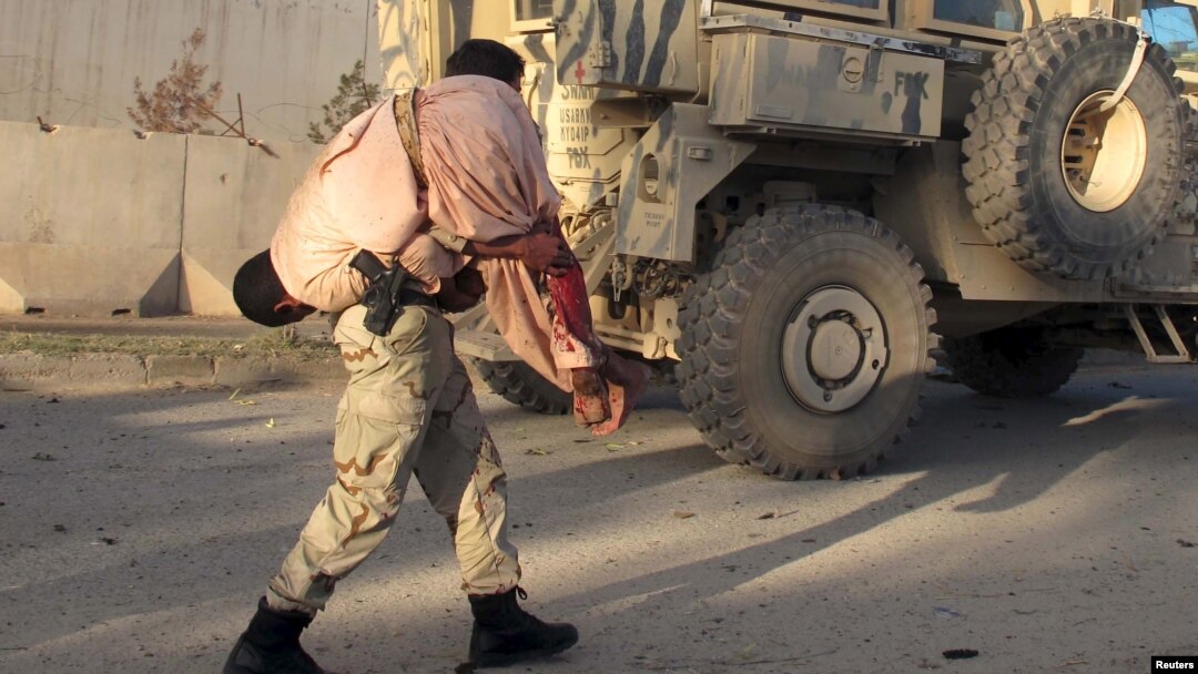 FILE - An Afghan security personnel carries a wounded man after a suicide car bomb blast attacked a military convoy in Lashkar Gah, Helmand province, Afghanistan, Nov. 15, 2015.