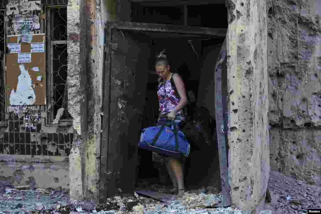 A woman walks out of a damaged multi-story block of flats carrying her belongings following what locals say was recent shelling by Ukrainian forces, in central Donetsk, July 29, 2014.