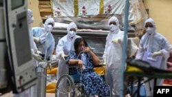 Nakes mengenakan APD berdiri di sekitar pasien yang menunggu untuk dipindahkan ke unit perawatan intensif (ICU), di pusat pemulihan pasien COVID-19, di Mumbai, 22 April 2021. (Punit PARANJPE / AFP)
