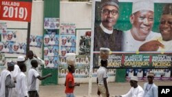 Street-vendors and others walk past a billboard showing Nigeria's President Muhammadu Buhari and other party officials, in Kano, northern Nigeria, Feb. 26, 2019. Buhari's election lead grew on Tuesday.