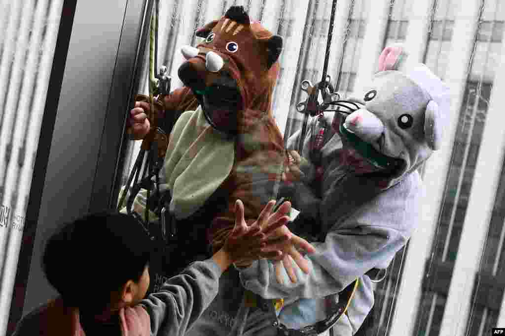 Workers wearing a pig and rat costume clean windows on a building in Tokyo, Dec. 19, 2019.