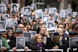 FILE— People hold up pictures of people who died during the bombing at the AMIA Jewish center that killed 85 people on the 25th anniversary of the attack in Buenos Aires, July 18, 2019.