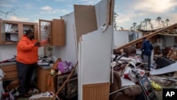 FILE - Granadas Baker, left, and son Granadas Jr., 18, right, retrieve personal items from the damaged home where they survived a tornado a day earlier in Beauregard, Alabama, March 4, 2019. 