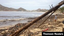 A woman walks through rubble and near a fallen lamppost on the beach after the crossing of Hurricane Genevieve in Cabo San Lucas, Mexico's Southern Baja Peninsula, Aug. 20, 2020.