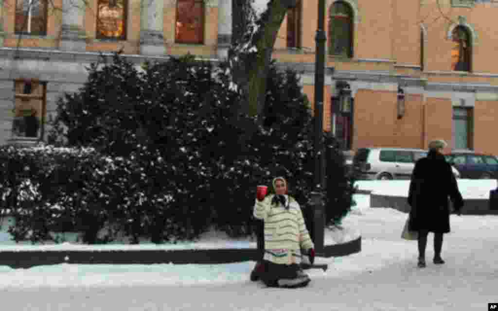 一女子在卡尔.约翰道上的国家剧院外跪地含笑乞讨。