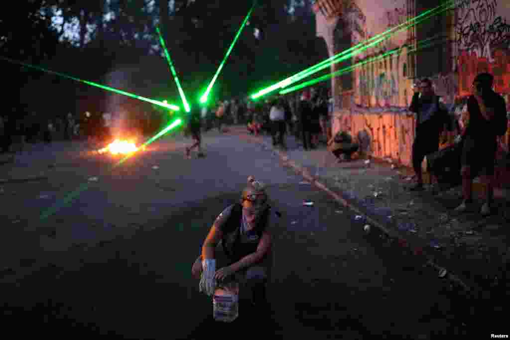 Laser lights are seen behind a demonstrator during a protest against Chile&#39;s government in Santiago, Chile, Nov. 18, 2019.