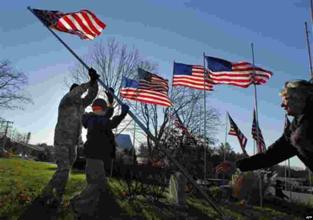 Chief Master Sgt. Bill Ross, a 35-year Air Force veteran, left, and Boy Scout Liam Gallagher, 12, raise one of 50 casket flags honoring local veterans, Thursday, Nov. 11, 2010, in Freeport, Maine. Glee Robinson Ross, right, helps guide the pole. (AP Photo
