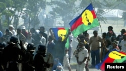 FILE - Pro-independance demonstrators hold a Kanak flags as they face French riot police during a protest outside the New Caledonian northern province assembly while [French President Jacques Chirac] was paying a visit to the New Caledonian northern city 