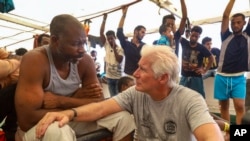 Actor Richard Gere, right, talks with migrants aboard the Open Arms Spanish humanitarian boat as it cruises in the Mediterranean Sea, Friday, Aug. 9, 2019. Open Arms has been carrying 121 migrants for a week in the central Mediterranean awaiting a…