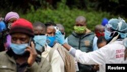 FILE - A health worker takes the temperature of a person standing in line for mass testing in an effort to stop the spread of the coronavirus disease (COVID-19) in the Kibera slum of Nairobi, Kenya, May 26, 2020. 