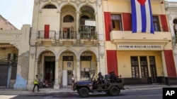 FILE - Special forces police patrol the streets as they drive past a large Cuban flag hanging from the facade of a building, in Havana, Cuba, July 21, 2021.