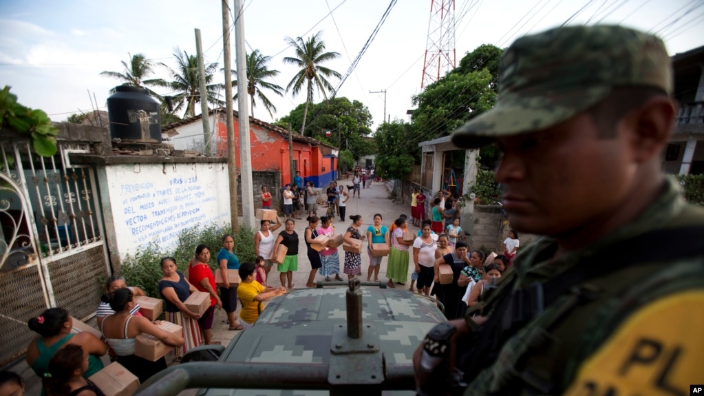 A soldier looks on as housewives stand in line for rations and water in Juchitan, Oaxaca state, Mexico, a zone heavily affected by Thursday's magnitude 8.1 earthquake, Sept. 9, 2017. 