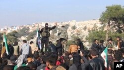 FILE - In this frame grab from video taken on Dec. 20, 2019, Hayat Tahrir al-Sham militants try to disperse people gathered at the Bab al-Hawa border gate to protest the ongoing bombing campaign in Syria's rebel-controlled Idlib province.