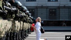 A woman kneels in front of a riot police line as they block Belarusian opposition supporters rally in the center of Minsk, Belarus.