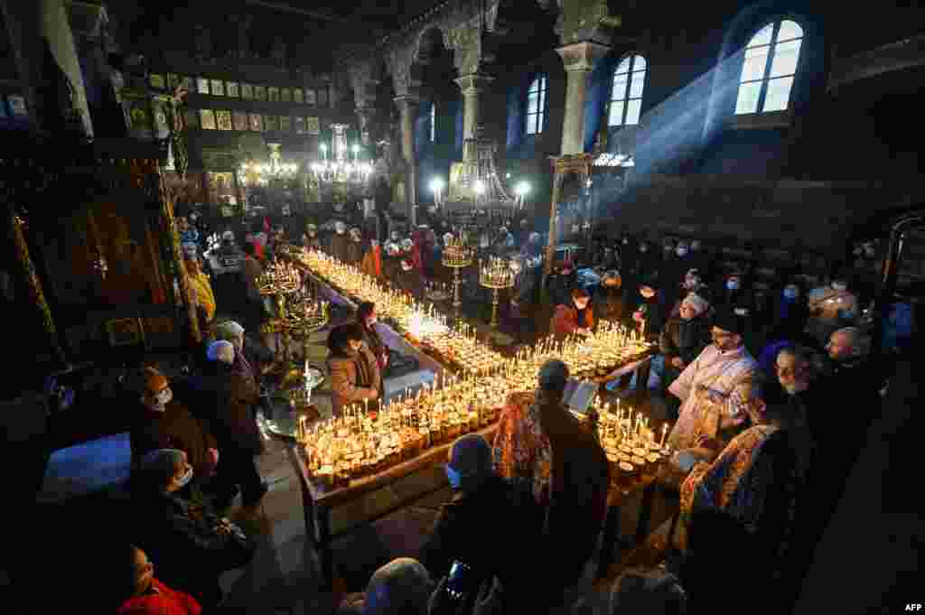 Believers pray around a cross-shaped platform covered with candles attached to jars of honey during a ceremony marking the day of Saint Haralampi, Orthodox patron saint of beekeepers, at the Church of the Blessed Virgin in Blagoevgrad, eastern Bulgaria.