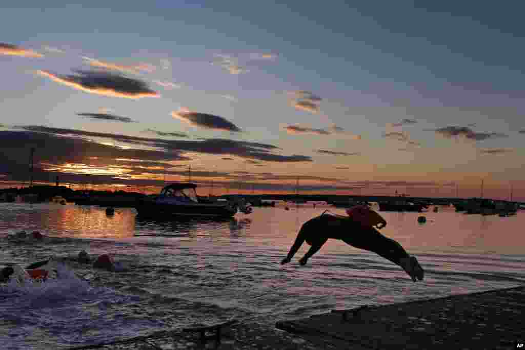 A long-distance swimmer dives into the Atlantic Ocean at dawn in Falmouth, Maine. The woman is part of a group that regularly starts their day with a two-mile swim. Many of the swimmers keep a float tethered to their bodies for safety.