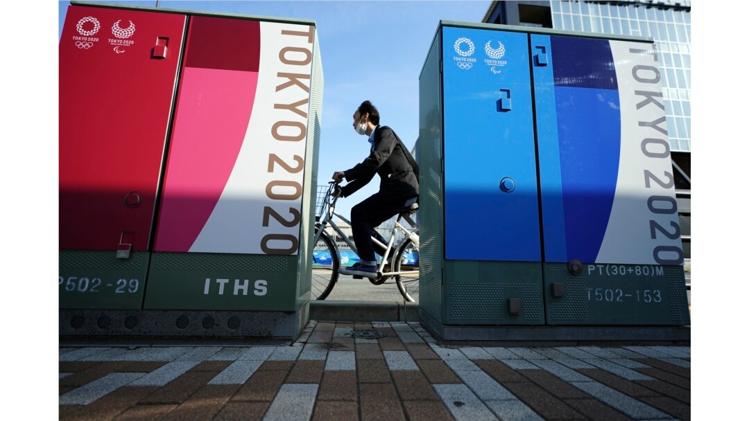Seorang pria mengendarai sepeda dengan mengenakan masker melewati beberapa iklan Olimpiade dan Paralimpiade Tokyo 2020 di Tokyo, Senin, 12 April 2021. (Foto AP / Eugene Hoshiko)