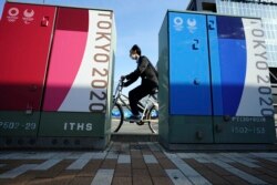 Seorang pria mengendarai sepeda dengan mengenakan masker melewati beberapa iklan Olimpiade dan Paralimpiade Tokyo 2020 di Tokyo, Senin, 12 April 2021. (Foto AP / Eugene Hoshiko)