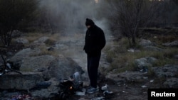 A smuggler, also known as a coyote, keeps warm by a fire on Christmas morning after guiding a group of migrants across into Eagle Pass, Texas, from Piedras Negras, Coahuila, Mexico, Dec. 25, 2023.