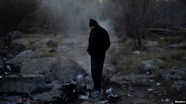 A smuggler, also known as a coyote, keeps warm by a fire on Christmas morning after guiding a group of migrants across into Eagle Pass, Texas, from Piedras Negras, Coahuila, Mexico, Dec. 25, 2023.