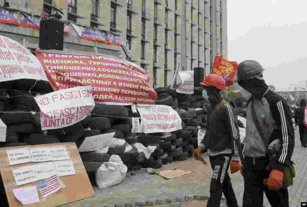 Masked pro-Russian activists pass by a barricade as they guard a regional administration building that they had seized earlier in Donetsk, Ukraine.