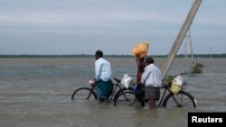 FILE - Sri Lankan men push their bicycles through flood waters after heavy rains in Batticaloa, about 320 km (199 miles) east of Colombo, Jan. 13, 2011. 